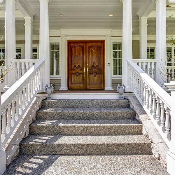 Entrance to a luxury country home with covered deck, white columns and staircase.